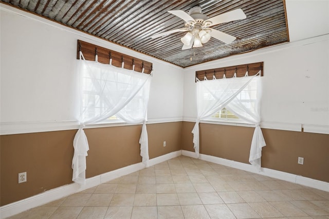 tiled empty room featuring ceiling fan and baseboards