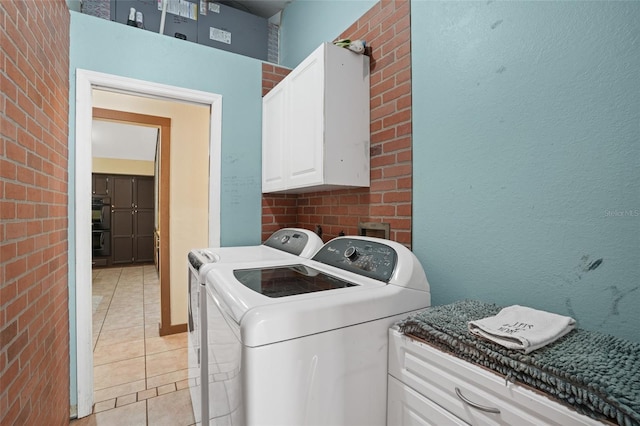 clothes washing area featuring light tile patterned floors, brick wall, separate washer and dryer, and cabinet space