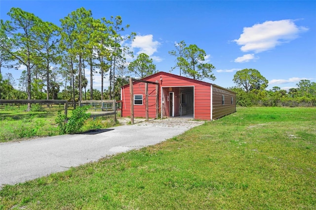 view of pole building featuring driveway, fence, and a lawn