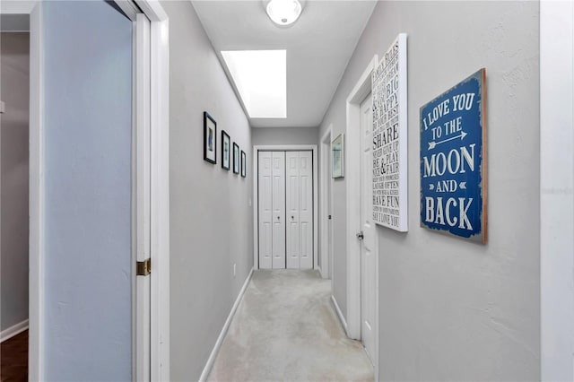 hallway featuring baseboards, a skylight, and carpet flooring