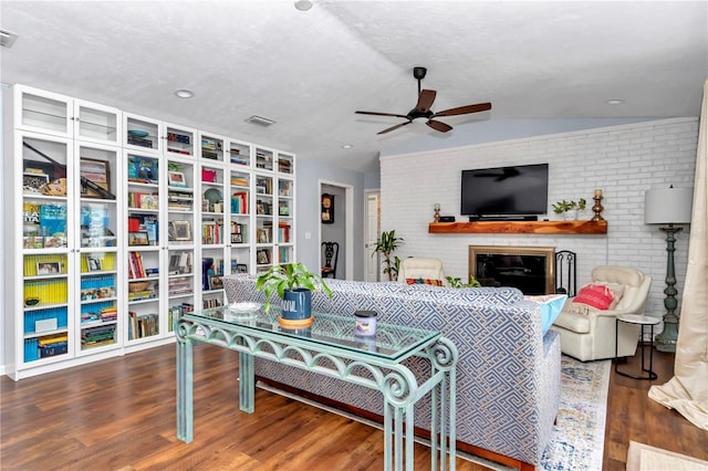 living area featuring vaulted ceiling, a fireplace, ceiling fan, and wood finished floors