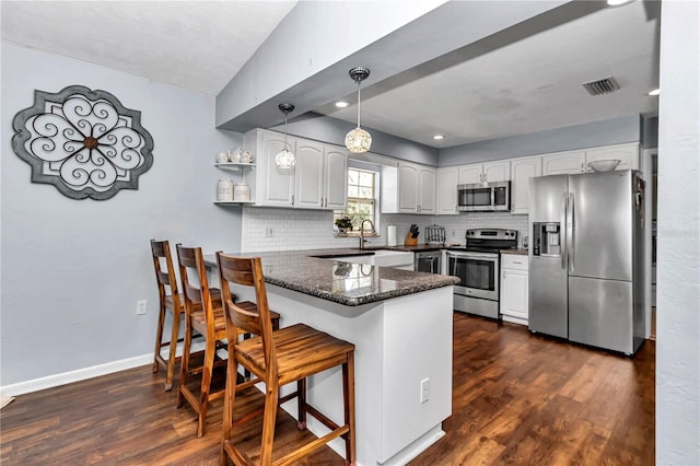 kitchen featuring backsplash, a peninsula, stainless steel appliances, and dark wood-type flooring