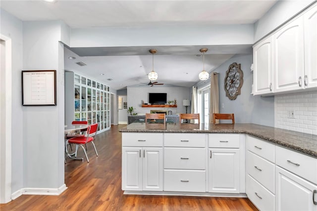 kitchen with dark wood-style floors, white cabinetry, a peninsula, lofted ceiling, and a brick fireplace