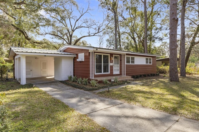 view of front of property featuring an attached carport, concrete driveway, a front lawn, and metal roof