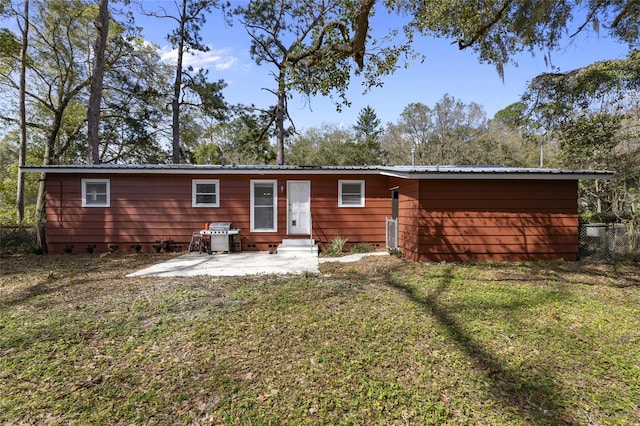 rear view of house with fence, entry steps, metal roof, a yard, and a patio