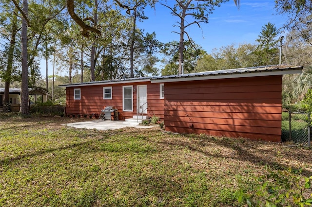 rear view of property featuring fence, entry steps, a patio area, a lawn, and metal roof