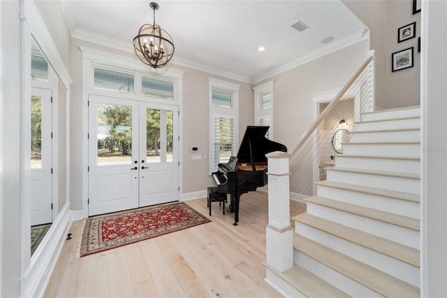 foyer entrance featuring visible vents, ornamental molding, stairway, an inviting chandelier, and light wood finished floors