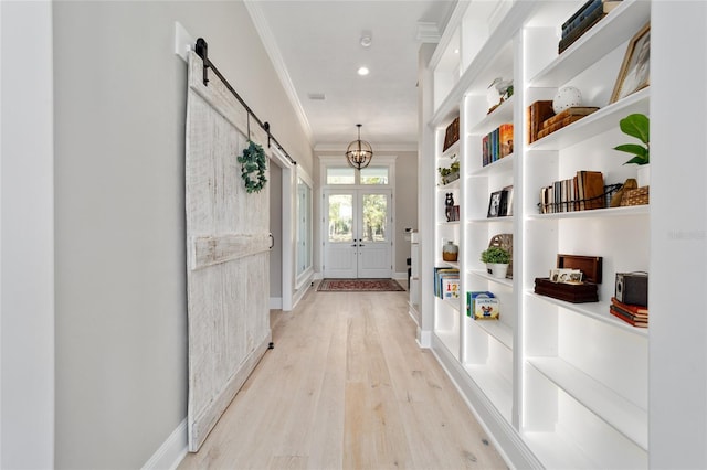 hallway with light wood finished floors, baseboards, a barn door, ornamental molding, and french doors