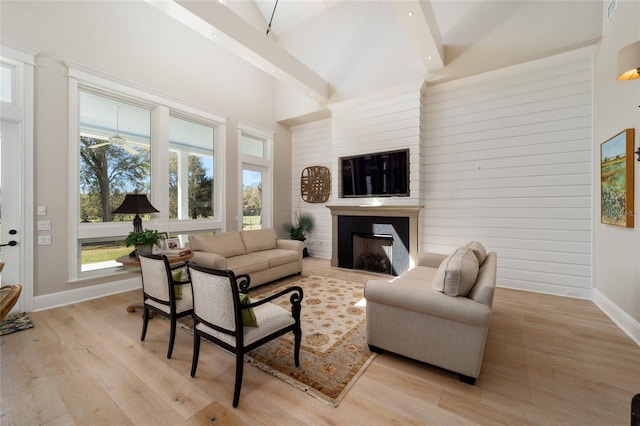 living area with baseboards, high vaulted ceiling, a healthy amount of sunlight, and light wood-style flooring