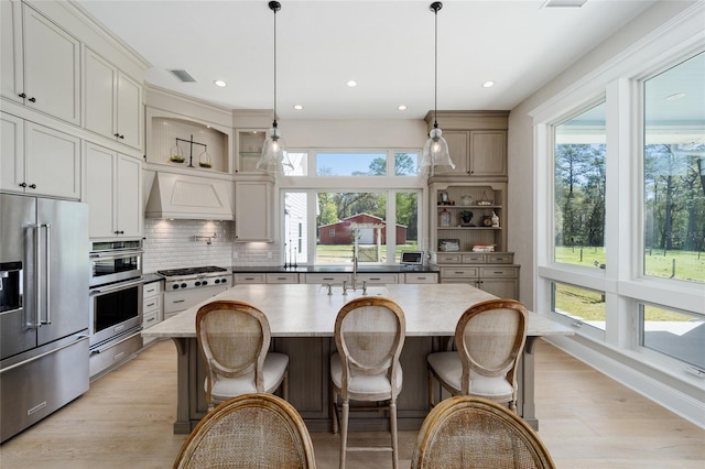 kitchen with light wood-type flooring, custom range hood, decorative backsplash, appliances with stainless steel finishes, and a warming drawer