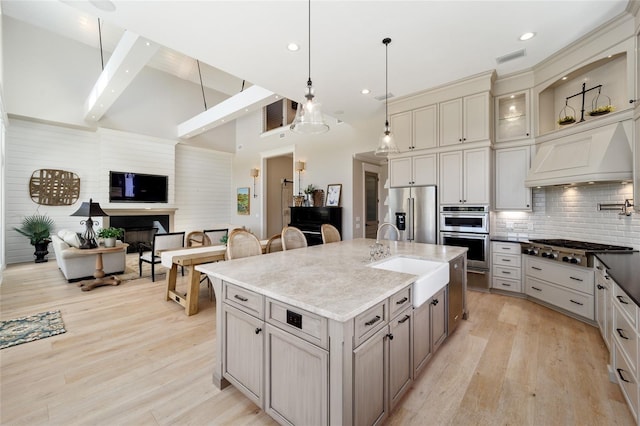 kitchen with gray cabinetry, light wood-style flooring, custom range hood, a sink, and stainless steel appliances