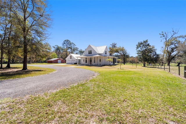 farmhouse inspired home featuring a front yard, fence, gravel driveway, an outdoor structure, and metal roof