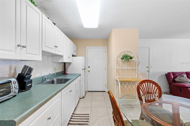 kitchen featuring a sink, a textured ceiling, freestanding refrigerator, white cabinets, and light tile patterned flooring