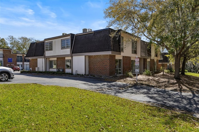 view of front of home featuring mansard roof, driveway, brick siding, and a front yard