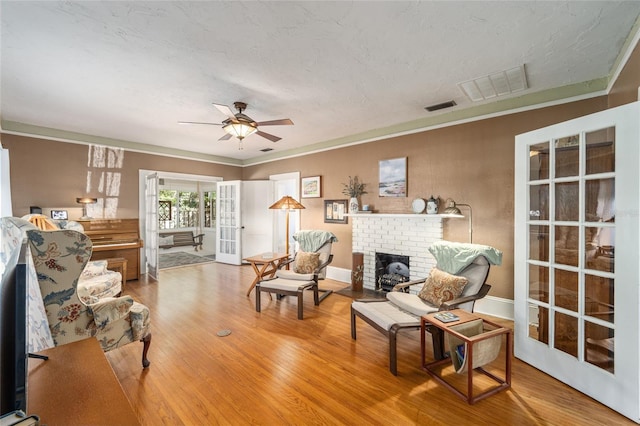 living area featuring a ceiling fan, wood finished floors, visible vents, and a fireplace