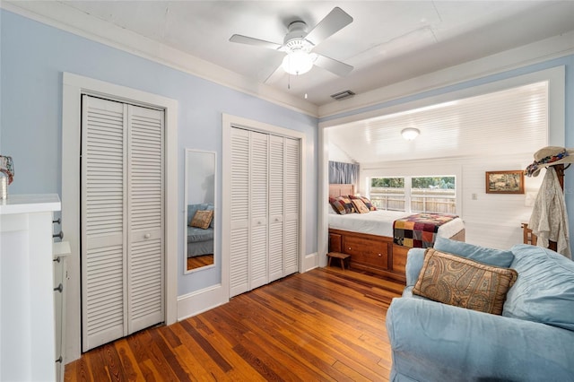 bedroom featuring crown molding, wood finished floors, visible vents, and two closets