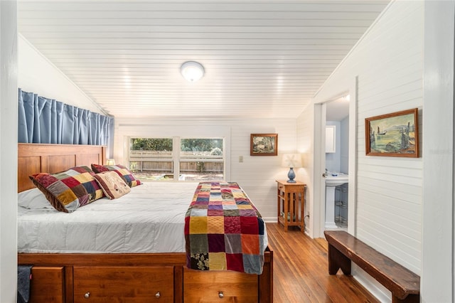 bedroom with ensuite bath, vaulted ceiling, and wood finished floors