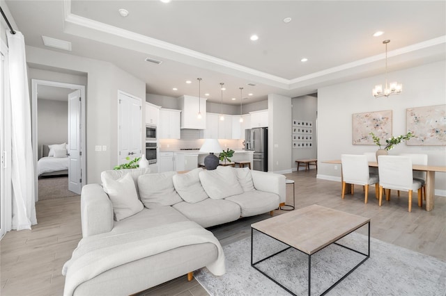 living area with a chandelier, recessed lighting, light wood-style flooring, and a tray ceiling