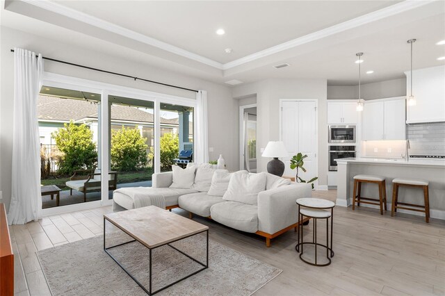 living room featuring visible vents, recessed lighting, ornamental molding, light wood-style floors, and a raised ceiling