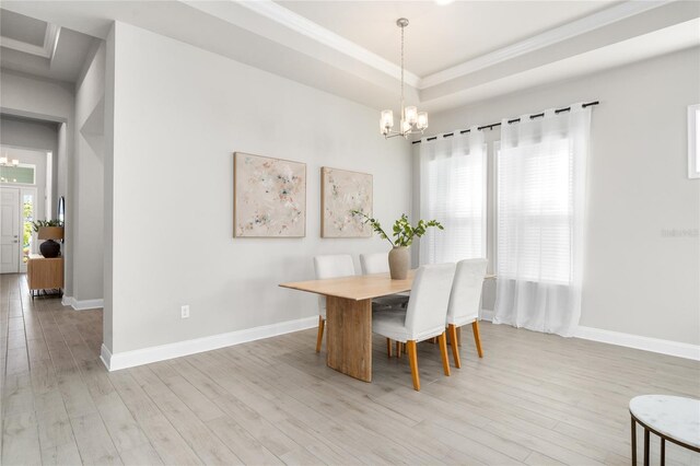 dining space featuring an inviting chandelier, baseboards, light wood-type flooring, and a raised ceiling