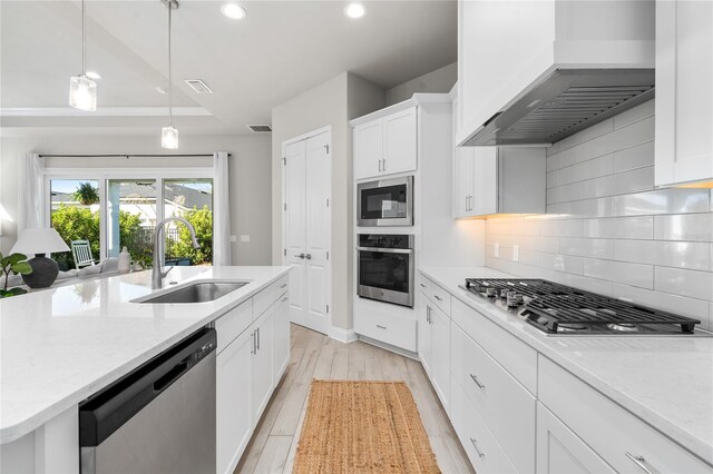 kitchen featuring light wood-type flooring, custom range hood, decorative backsplash, stainless steel appliances, and a sink