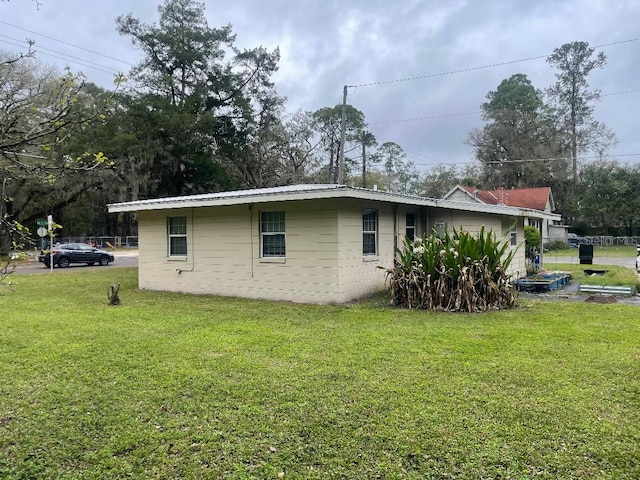 view of side of property with a lawn, concrete block siding, and metal roof