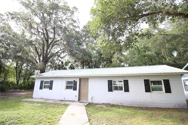 ranch-style home with concrete block siding, a front lawn, and metal roof