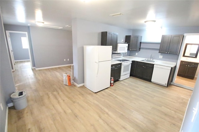 kitchen featuring baseboards, light countertops, light wood-type flooring, white appliances, and a sink