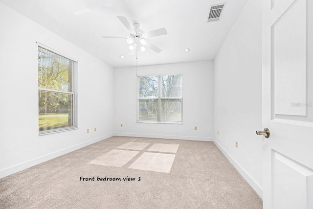 spare room with ceiling fan, light colored carpet, visible vents, and baseboards