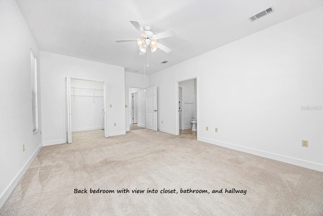 unfurnished bedroom featuring visible vents, a walk in closet, ensuite bath, baseboards, and light colored carpet