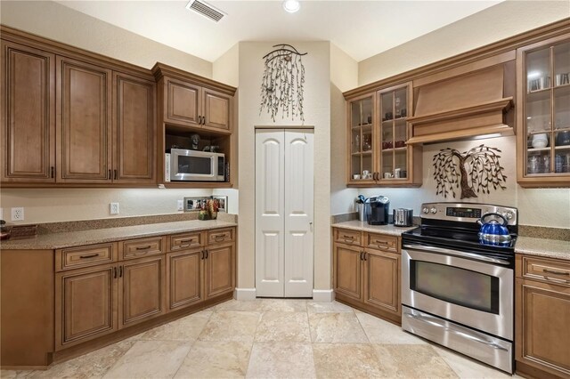 kitchen featuring visible vents, custom range hood, glass insert cabinets, appliances with stainless steel finishes, and brown cabinets