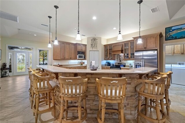 kitchen featuring visible vents, stainless steel appliances, custom range hood, glass insert cabinets, and independent washer and dryer