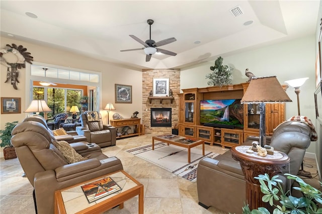 living area featuring a stone fireplace, visible vents, a tray ceiling, and ceiling fan