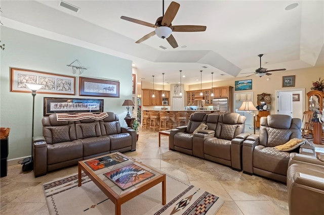 living room with a tray ceiling, baseboards, visible vents, and ceiling fan