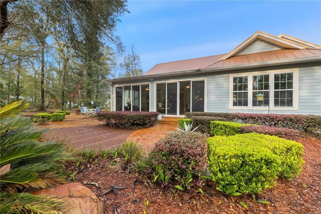 back of house featuring metal roof, a standing seam roof, and a sunroom