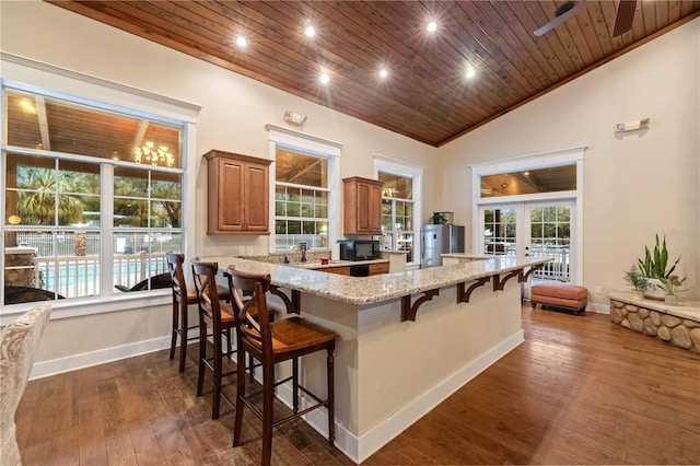 kitchen featuring light stone counters, french doors, wood ceiling, black microwave, and a kitchen breakfast bar