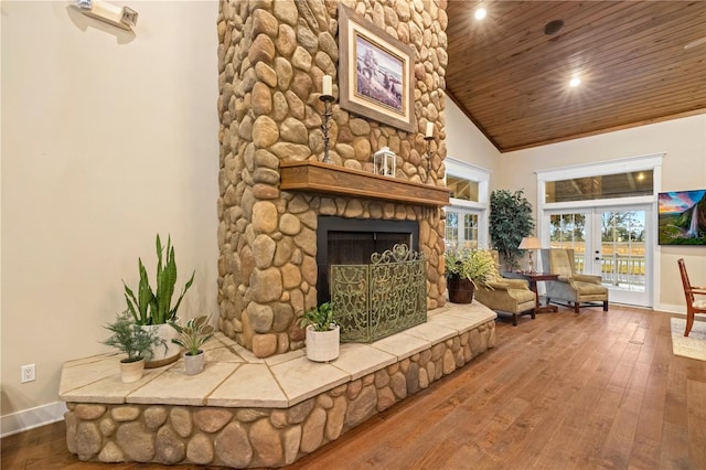 living area featuring a stone fireplace, vaulted ceiling, wood ceiling, french doors, and wood-type flooring