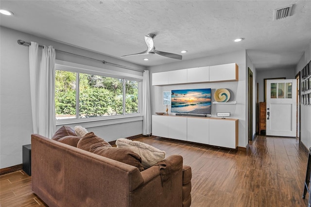 living room featuring visible vents, a textured ceiling, wood finished floors, baseboards, and ceiling fan