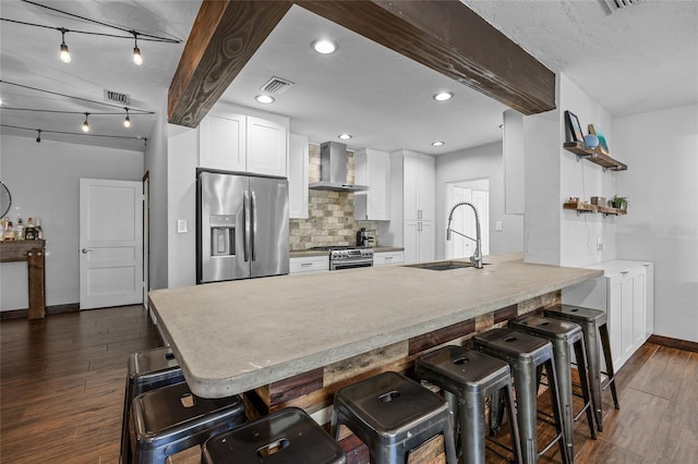 kitchen with dark wood finished floors, a peninsula, a sink, stainless steel appliances, and wall chimney exhaust hood