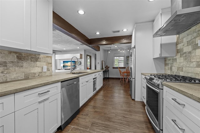 kitchen with wall chimney range hood, appliances with stainless steel finishes, dark wood-style floors, white cabinetry, and a sink