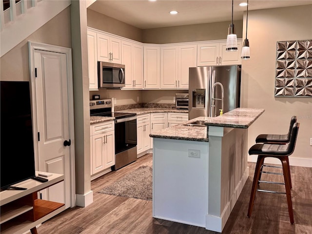 kitchen featuring white cabinets, wood finished floors, a center island with sink, and stainless steel appliances