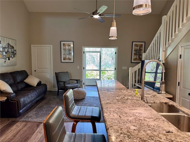 living room with stairway, a ceiling fan, a towering ceiling, and wood finished floors