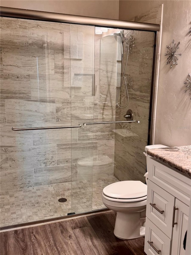 full bathroom featuring vanity, toilet, wood finished floors, and a stall shower