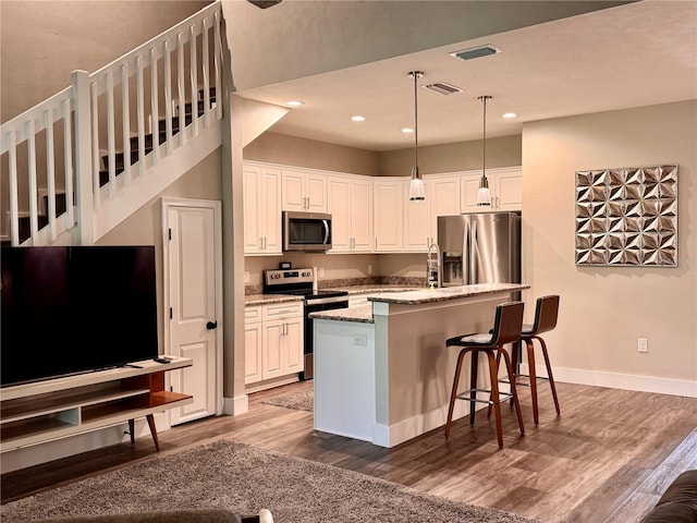 kitchen with wood finished floors, visible vents, stainless steel appliances, white cabinetry, and decorative light fixtures