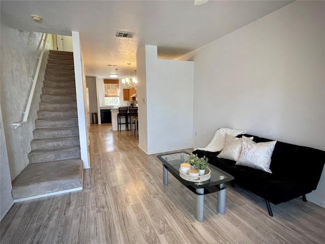 living room featuring light wood-type flooring, visible vents, a notable chandelier, and stairway