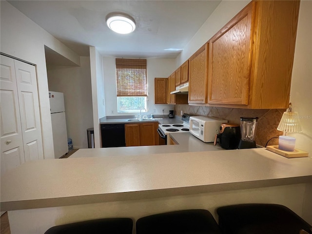 kitchen featuring white appliances, a peninsula, a sink, decorative backsplash, and under cabinet range hood