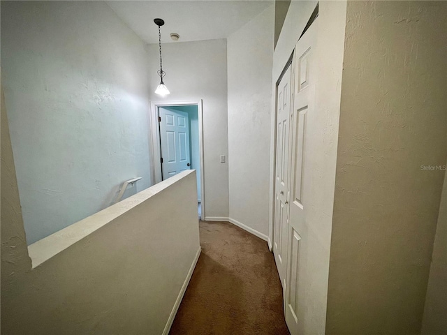 corridor with an upstairs landing, a textured wall, baseboards, and dark carpet