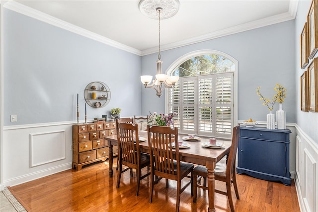 dining area featuring a decorative wall, ornamental molding, wainscoting, wood finished floors, and a notable chandelier