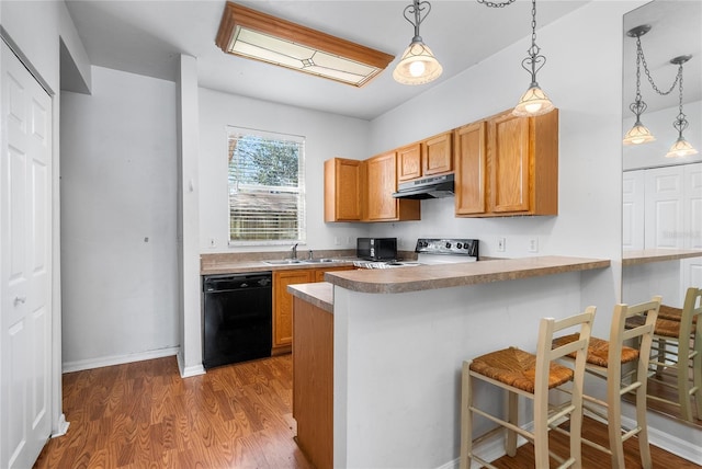 kitchen featuring wood finished floors, a sink, black appliances, under cabinet range hood, and a kitchen breakfast bar