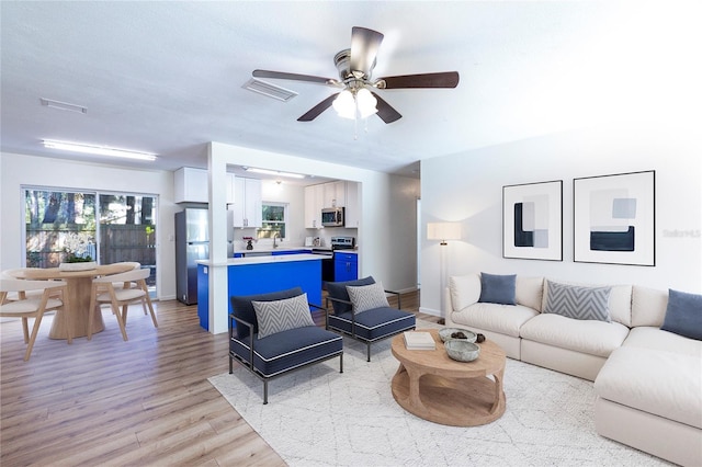 living room featuring light wood-type flooring, visible vents, baseboards, and a ceiling fan